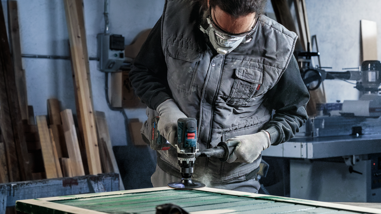 Una persona che indossa un equipaggiamento di sicurezza lucida una superficie di legno con un utensile elettrico.