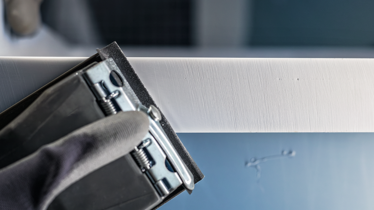 Una persona che indossa un equipaggiamento di sicurezza leviga un bordo bianco con uno strumento abrasivo.