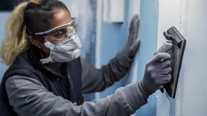 Persona che indossa dispositivi di sicurezza mentre carteggia un muro.