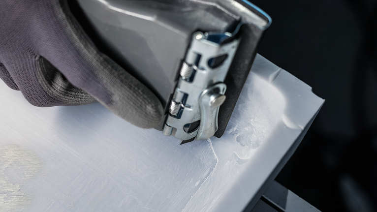 Una persona che indossa un equipaggiamento di sicurezza utilizza un elettroutensile per levigare il bordo di un materiale bianco.