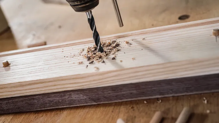 Praticare un foro su una tavola di legno con trucioli di legno attorno alla punta.