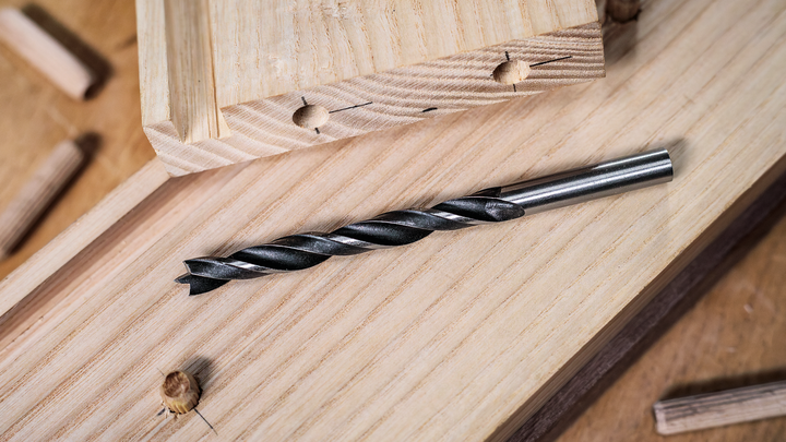 Punta del trapano posizionata su assi di legno con tasselli nelle vicinanze.