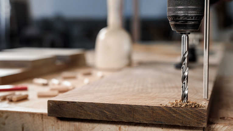 Un trapano elettrico pratica un foro in una tavola di legno su un banco da lavoro.