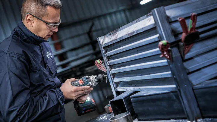 Una persona che indossa un equipaggiamento di sicurezza fora un telaio di ventilazione in metallo in un'officina.