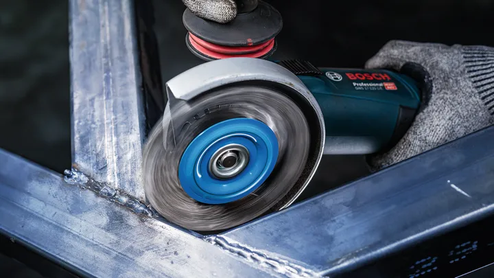 Una persona che indossa un equipaggiamento di sicurezza leviga l'angolo di un telaio metallico con una smerigliatrice angolare.