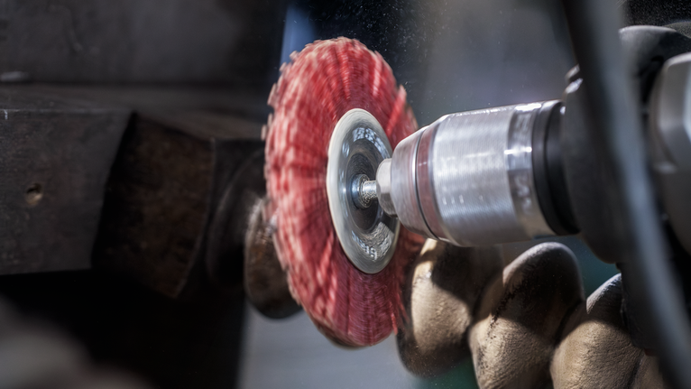 La persona che indossa l'equipaggiamento di sicurezza utilizza un elettroutensile con un disco abrasivo rosso sul metallo.