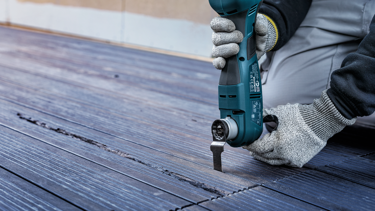 Una persona che indossa dispositivi di sicurezza utilizza un elettroutensile per tagliare il pavimento in legno.