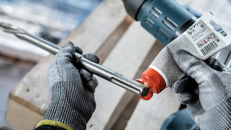 Una persona che indossa un equipaggiamento di sicurezza applica del lubrificante alla punta di un trapano.