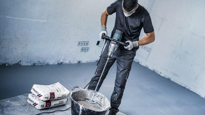 Una persona che indossa dispositivi di sicurezza mescola la polvere di cemento in un secchio in un cantiere edile.