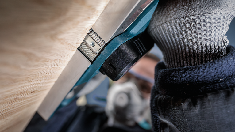 Una persona che indossa dispositivi di sicurezza utilizza un elettroutensile vicino a una superficie di legno.