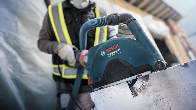 Una persona che indossa un equipaggiamento di sicurezza utilizza uno scanalatore per tagliare il cemento.