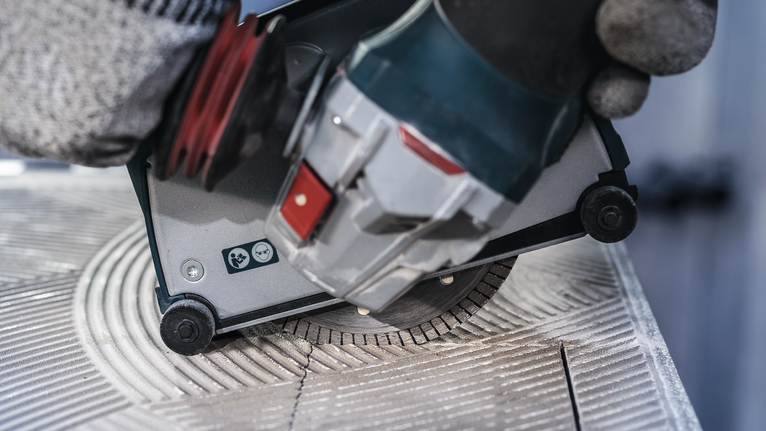 Una persona che indossa dispositivi di sicurezza utilizza una sega circolare per tagliare una piastrella di ceramica.