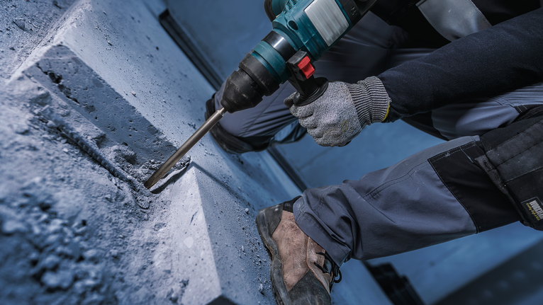 Una persona che indossa un equipaggiamento di sicurezza perfora il cemento con un martello perforatore.