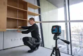 Una persona installa uno scaffale utilizzando uno strumento di livellamento laser per garantirne l'allineamento.