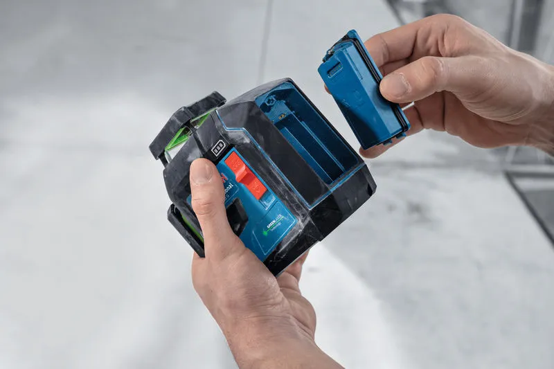 Una persona inserisce una batteria in uno strumento di livellamento laser in un cantiere edile.