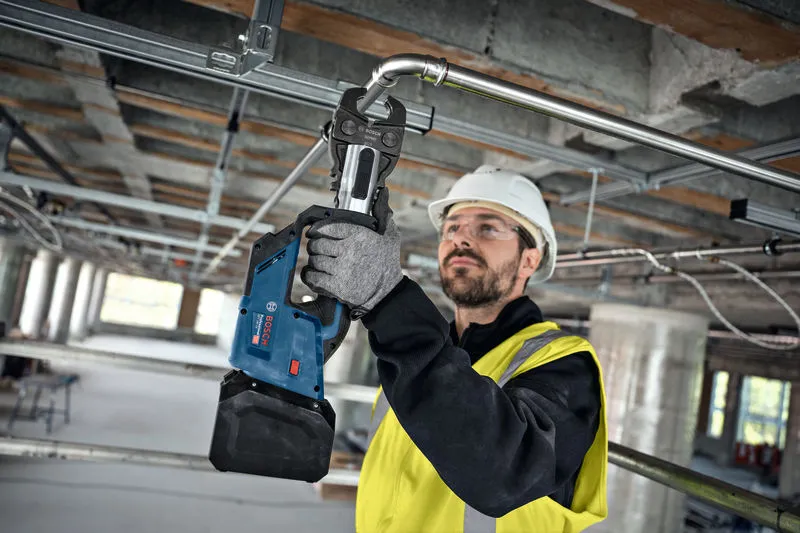 Una persona che indossa un equipaggiamento di sicurezza utilizza una pressa senza fili su un tubo metallico.