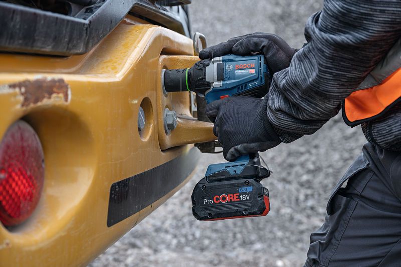 Una persona che indossa dispositivi di sicurezza utilizza una chiave a impulsi a batteria su macchinari pesanti.