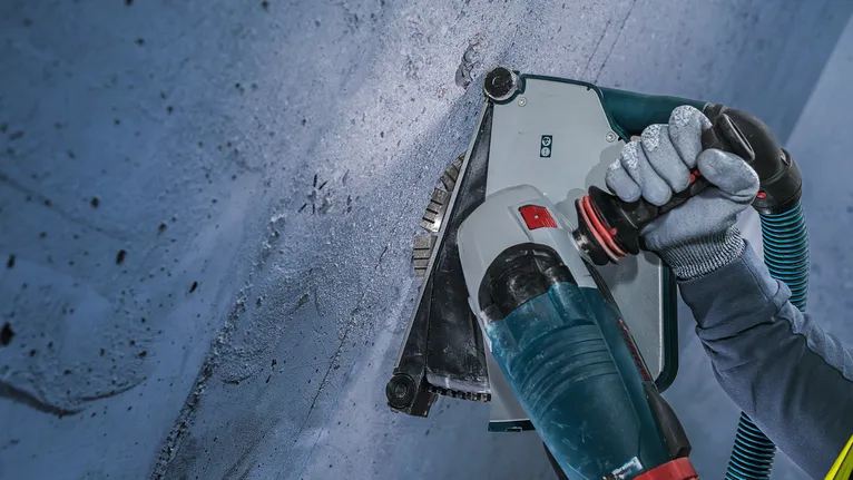 Una persona che indossa un equipaggiamento di sicurezza pratica una scanalatura nel cemento con un elettroutensile.