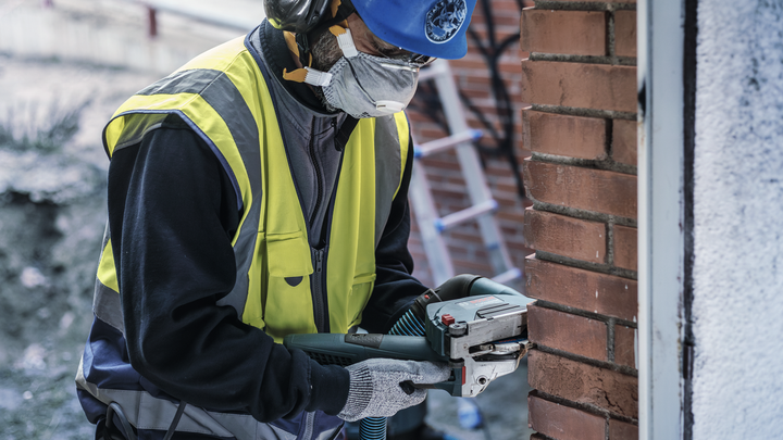 Una persona che indossa un equipaggiamento di sicurezza taglia un muro di mattoni utilizzando un elettroutensile.
