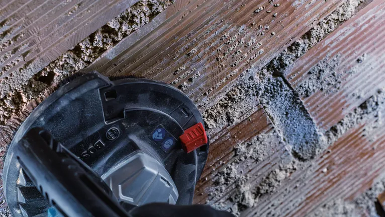 Una persona che indossa un equipaggiamento di sicurezza scava un canale in un muro di cemento.