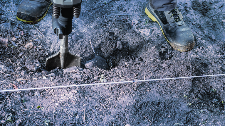 Un lavoratore che indossa dispositivi di sicurezza utilizza un martello demolitore per rompere il terreno.