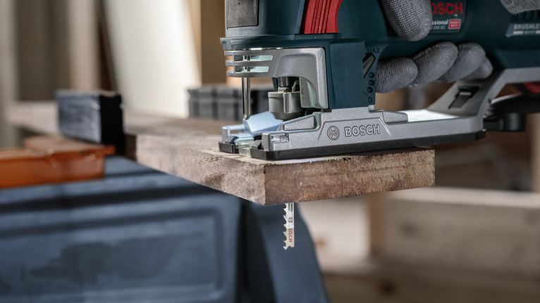 Una persona che indossa dispositivi di sicurezza usa un seghetto alternativo per tagliare una tavola di legno.