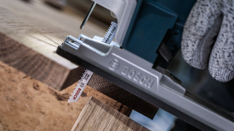 Una persona che indossa dispositivi di sicurezza usa un seghetto alternativo per tagliare una tavola di legno.