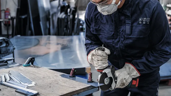 Una persona che indossa un equipaggiamento di sicurezza utilizza una smerigliatrice per tagliare lamiere.