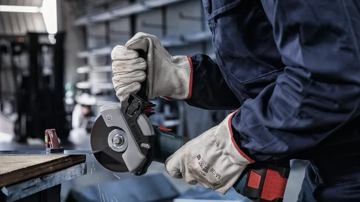 Persona che indossa dispositivi di sicurezza mentre taglia il metallo con una smerigliatrice manuale.