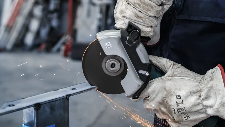 Una persona che indossa dispositivi di sicurezza taglia il metallo con una sega circolare, creando scintille.