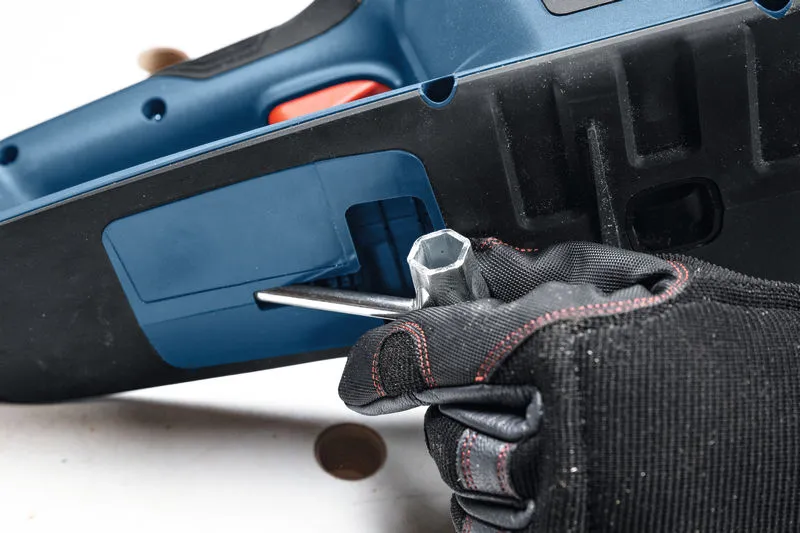 Una persona che indossa un equipaggiamento di sicurezza utilizza una chiave inglese per regolare una motosega a batteria.