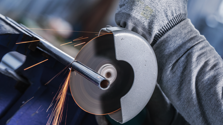 Persona che indossa dispositivi di sicurezza mentre taglia un tubo metallico con un utensile per rettifica.