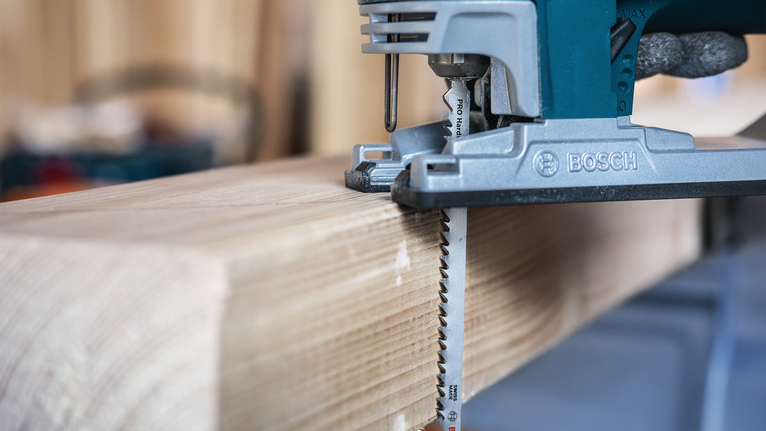 Una persona taglia una spessa trave di legno con un seghetto alternativo in un'officina.