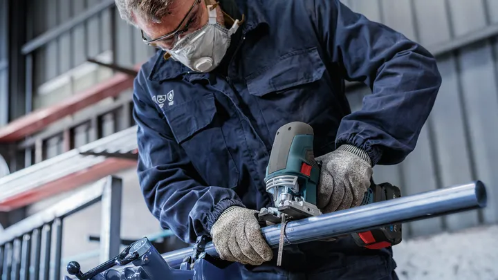 Una persona che indossa un equipaggiamento di sicurezza taglia un tubo di metallo con un seghetto alternativo.