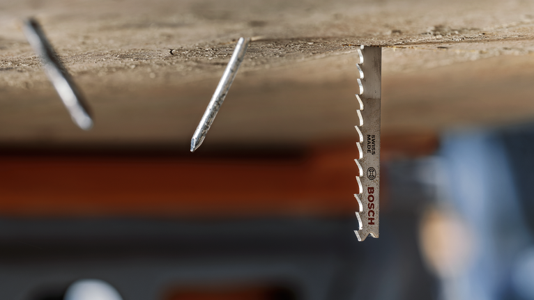 Una lama di sega metallica installata nel legno accanto a due chiodi sporgenti.