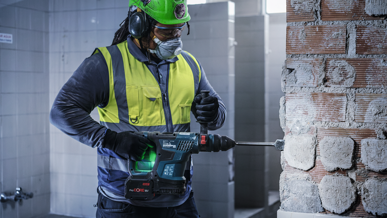 Una persona che indossa un equipaggiamento di sicurezza fora un muro di mattoni in un ambiente interno.