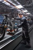 Una persona che indossa un equipaggiamento di sicurezza utilizza un avvitatore a impulsi per assemblare il telaio di una motocicletta.