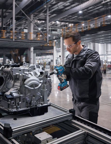 Una persona che indossa un equipaggiamento di sicurezza utilizza una chiave a impulsi senza fili su un gruppo motore.