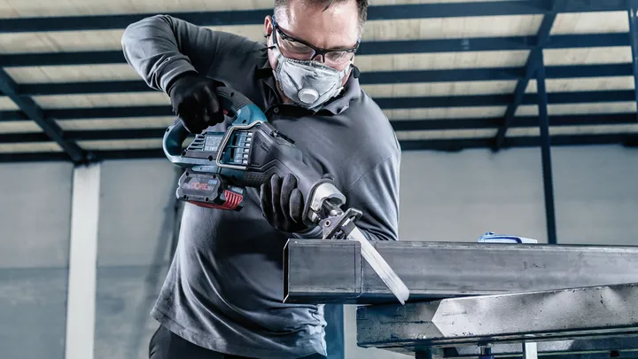 Una persona che indossa un equipaggiamento di sicurezza usa un seghetto alternativo per tagliare una trave metallica.