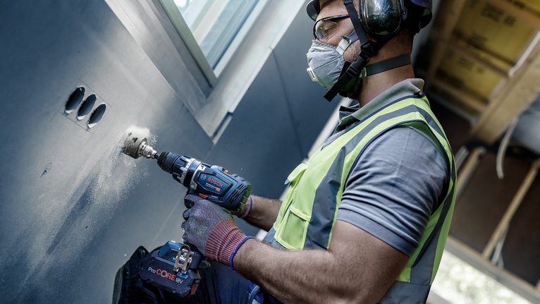 Una persona che indossa un equipaggiamento di sicurezza pratica un foro nel muro.