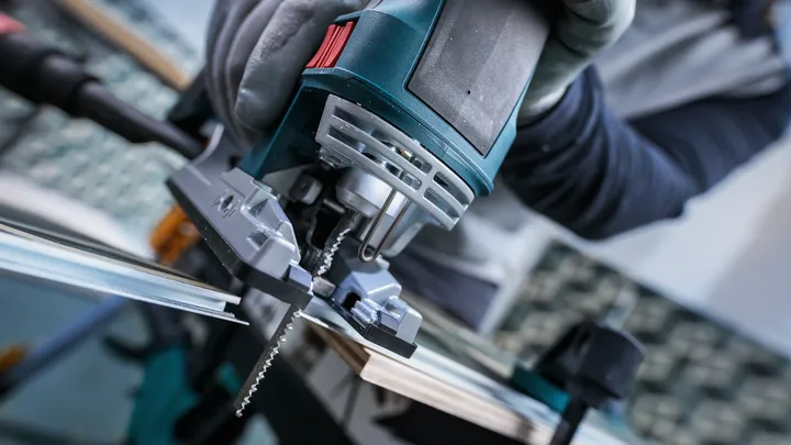 Persona che indossa dispositivi di sicurezza mentre usa un seghetto alternativo per tagliare una tavola di legno.