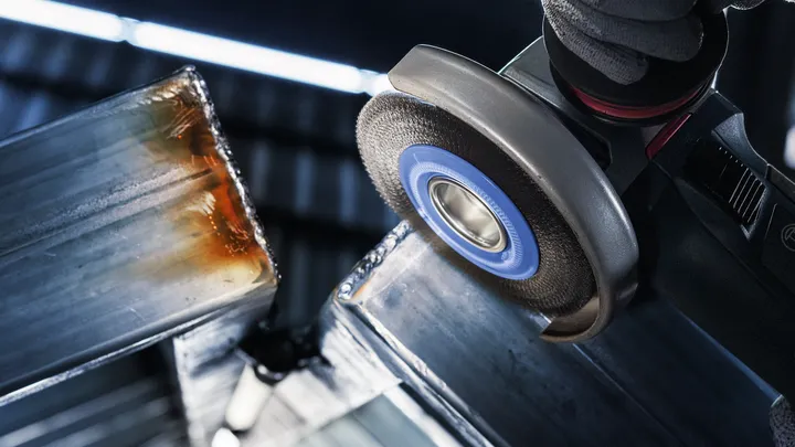 Una persona che indossa l'equipaggiamento di sicurezza smeriglia il bordo di una trave metallica.