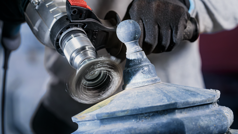 Una persona che indossa un equipaggiamento di sicurezza lucida un apparecchio metallico con un utensile elettrico.