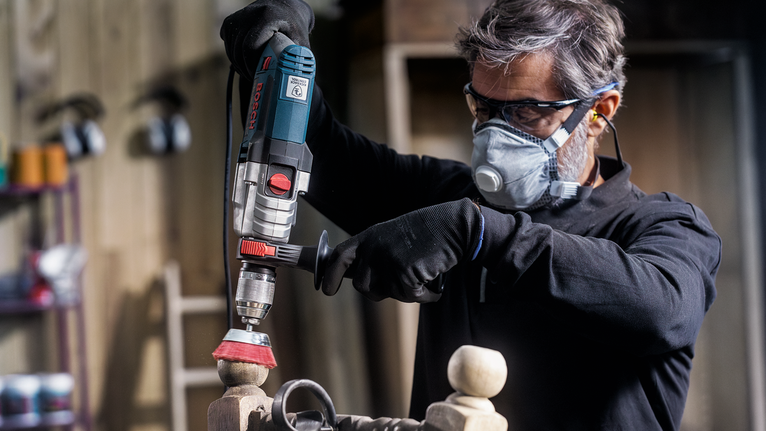 Una persona che indossa un equipaggiamento di sicurezza lucida un palo di legno con un utensile elettrico.