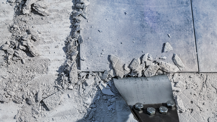 Uno scalpello rompe piastrelle di ceramica e detriti su un pavimento polveroso.