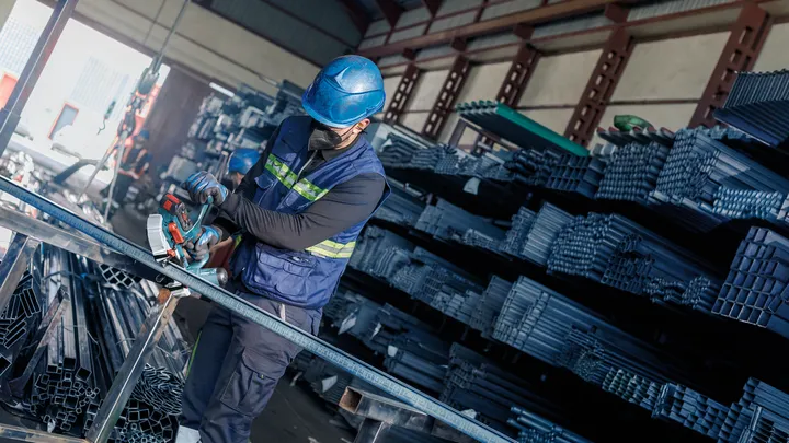 Una persona che indossa dispositivi di sicurezza taglia tubi metallici in un magazzino.