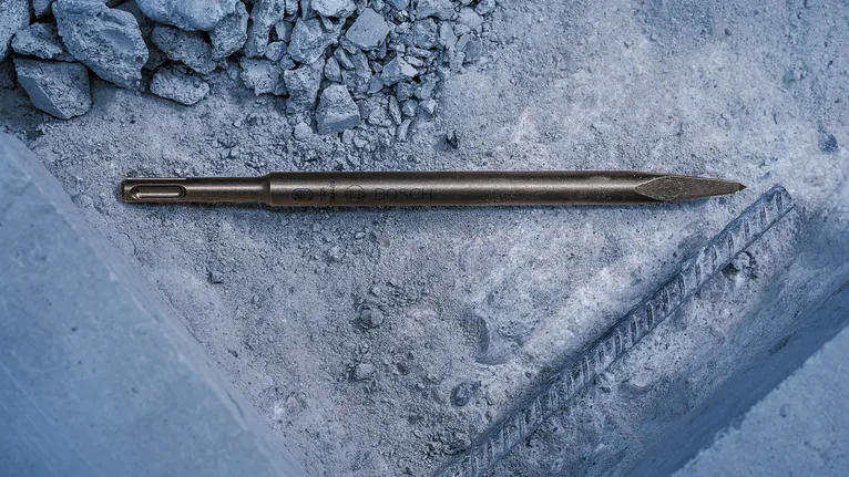 Scalpello appuntito appoggiato su macerie di cemento in un cantiere edile.