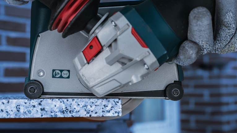 Una persona che indossa un equipaggiamento di sicurezza taglia una lastra di granito con una sega elettrica.