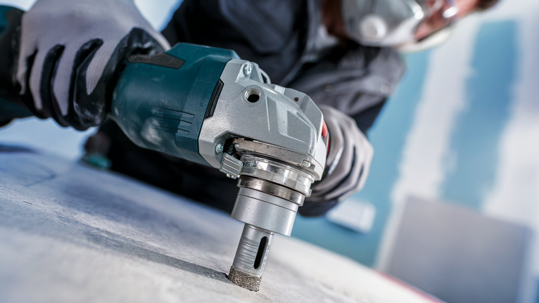 Una persona che indossa un equipaggiamento di sicurezza fora il cemento con un utensile elettrico.