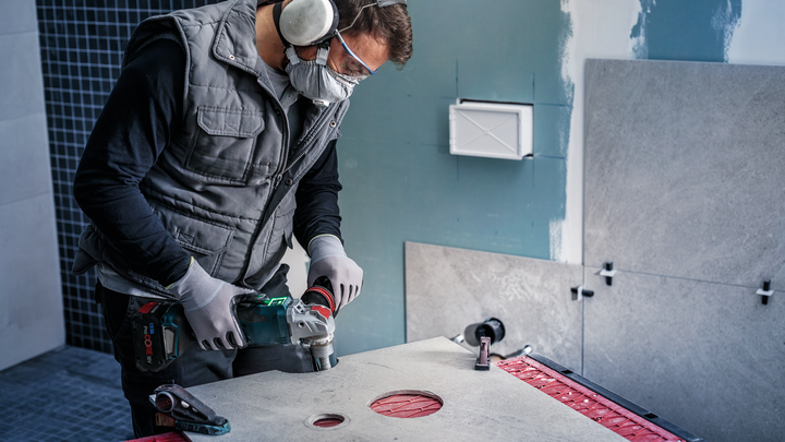 Una persona che indossa un equipaggiamento di sicurezza pratica un foro circolare sul piano di lavoro con un elettroutensile.